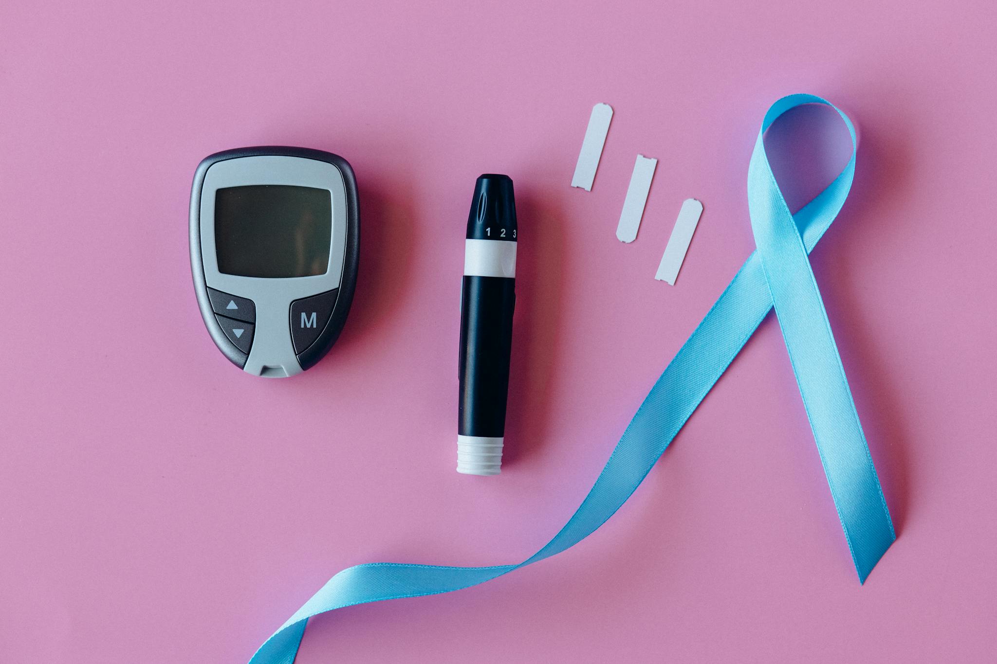 A glucometer with blue ribbon for diabetes awareness on a pink background.