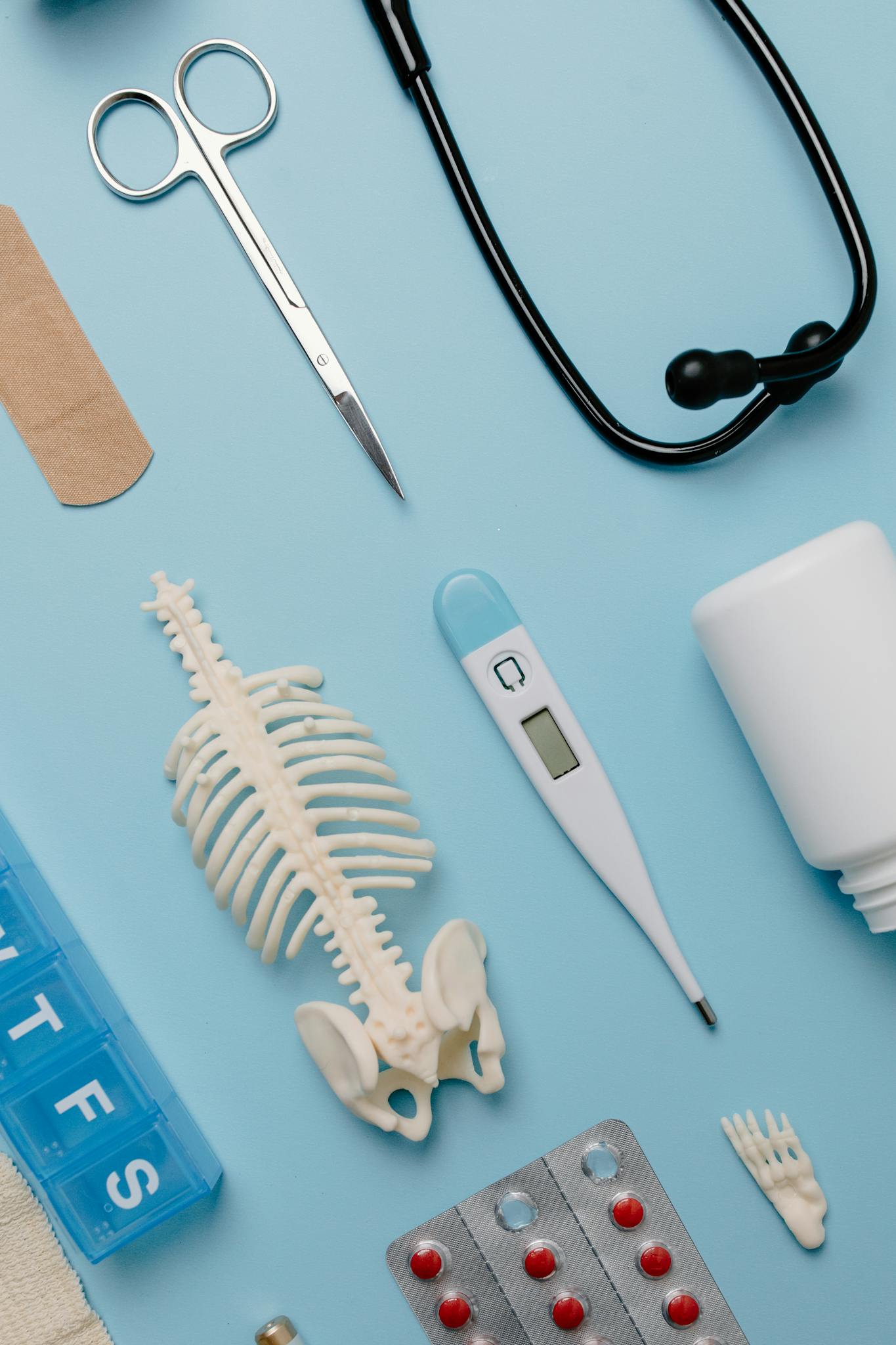 Flat lay of medical tools and skeleton model on a blue background.